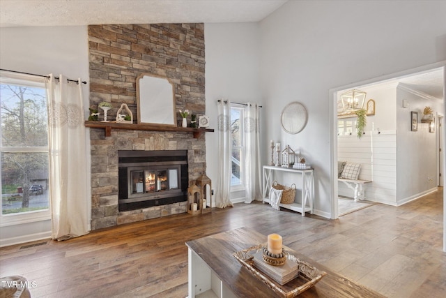 living area featuring high vaulted ceiling, wood finished floors, a stone fireplace, baseboards, and visible vents