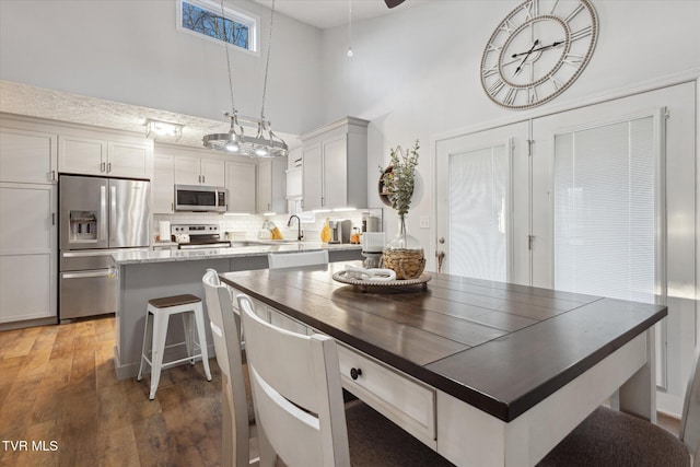 interior space with tasteful backsplash, light wood-type flooring, a center island, a towering ceiling, and appliances with stainless steel finishes