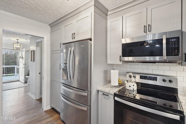 kitchen with an inviting chandelier, stainless steel appliances, a textured ceiling, decorative backsplash, and wood finished floors