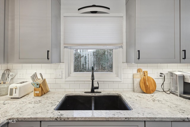 kitchen featuring a sink, tasteful backsplash, light stone counters, and gray cabinetry