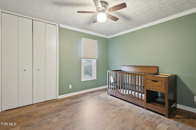 bedroom featuring ornamental molding, baseboards, a textured ceiling, a closet, and wood finished floors