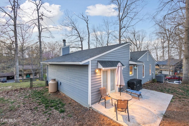 rear view of house featuring fence, a chimney, a patio area, and roof with shingles