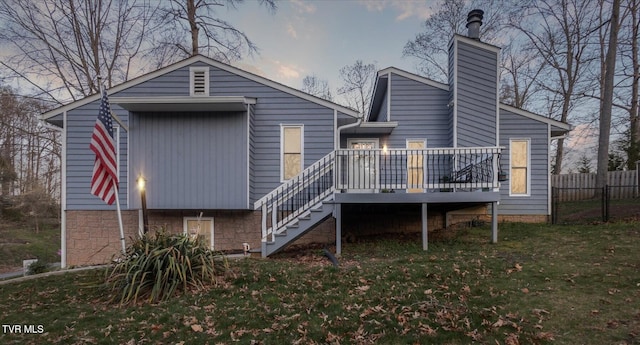 back of property featuring stairs, a chimney, a wooden deck, fence, and a lawn