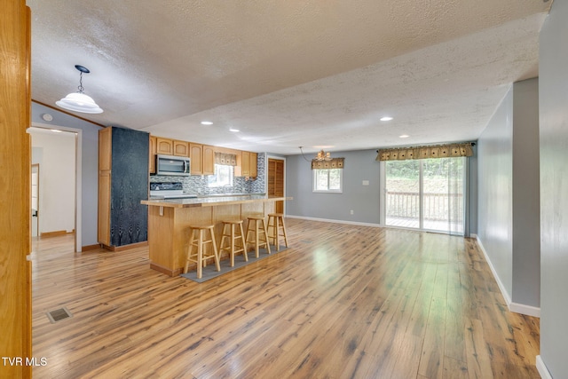 kitchen featuring a breakfast bar area, a textured ceiling, stainless steel microwave, and light wood-style floors