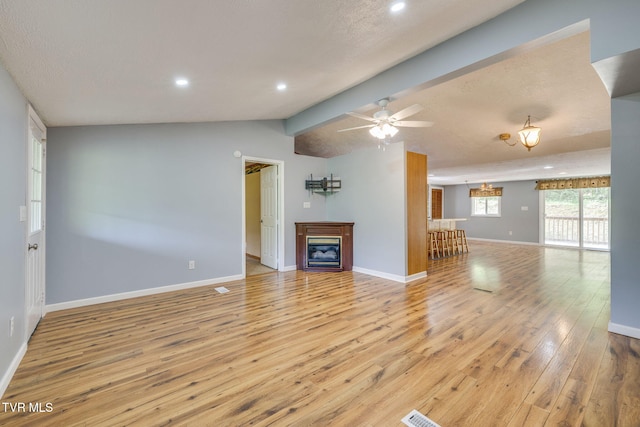 unfurnished living room featuring a ceiling fan, a glass covered fireplace, baseboards, lofted ceiling with beams, and light wood finished floors