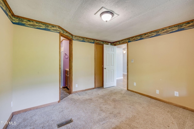 carpeted spare room with visible vents, a textured ceiling, and baseboards