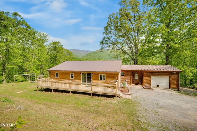 log-style house featuring gravel driveway, a deck with mountain view, a front lawn, and a garage