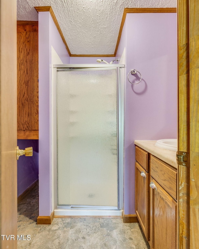 full bath with vanity, a textured ceiling, baseboards, ornamental molding, and a stall shower