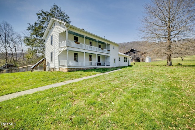 back of property featuring covered porch, a balcony, and a yard