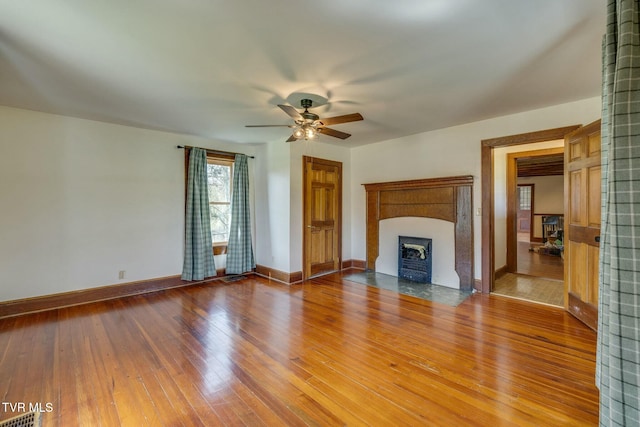 unfurnished living room featuring a fireplace with flush hearth, baseboards, hardwood / wood-style flooring, visible vents, and a ceiling fan