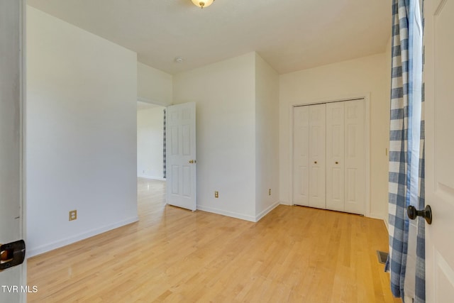 unfurnished bedroom with light wood-style flooring, a closet, and baseboards