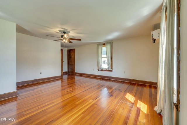 spare room featuring a ceiling fan, an AC wall unit, light wood-style floors, and baseboards