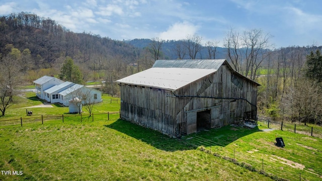 view of barn featuring a lawn, fence, and a forest view