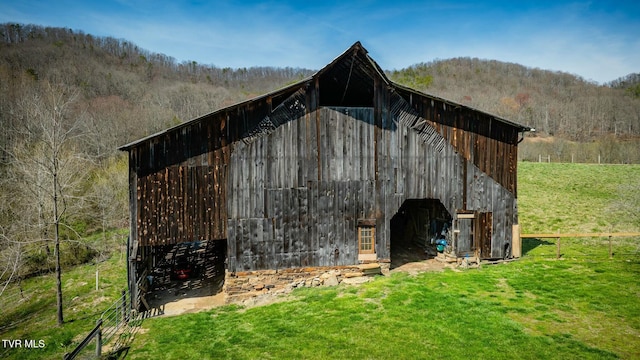 view of barn with a lawn, fence, and a view of trees