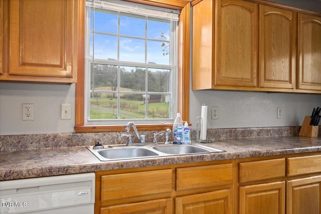 kitchen with brown cabinets, dark countertops, a sink, and dishwasher