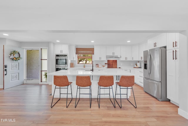 kitchen featuring a kitchen breakfast bar, white cabinets, appliances with stainless steel finishes, light countertops, and light wood finished floors