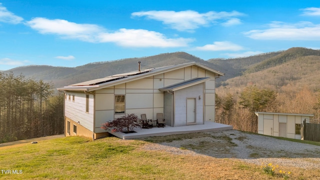 back of house featuring solar panels, driveway, a mountain view, a yard, and a patio area