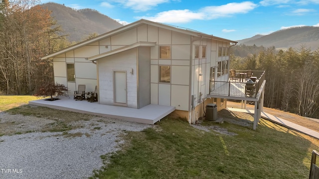 back of property featuring a deck with mountain view, central air condition unit, a patio area, and a lawn