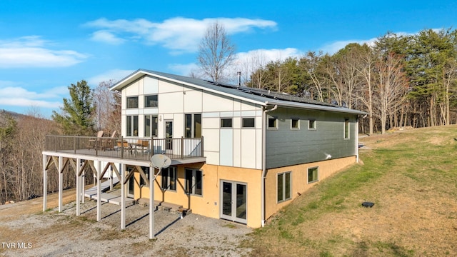 rear view of property with a wooden deck, solar panels, stucco siding, french doors, and a yard