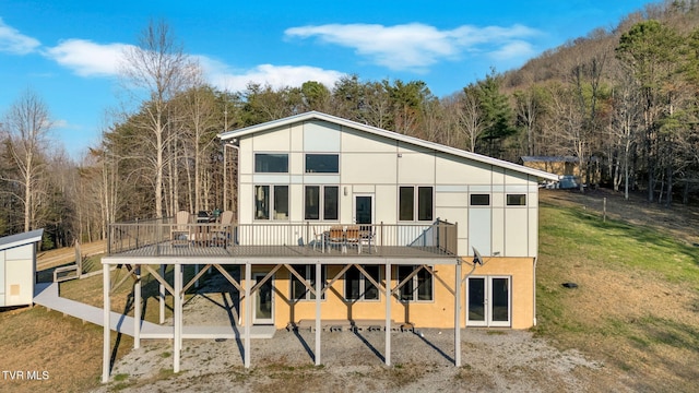 back of house featuring french doors, a wooden deck, stucco siding, and a lawn