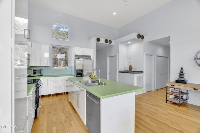 kitchen featuring white cabinetry, stainless steel appliances, backsplash, a sink, and light wood-style flooring