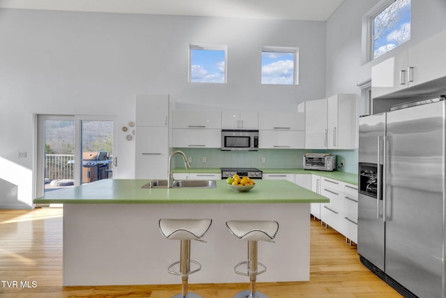 kitchen featuring stainless steel appliances, a high ceiling, a sink, white cabinets, and modern cabinets