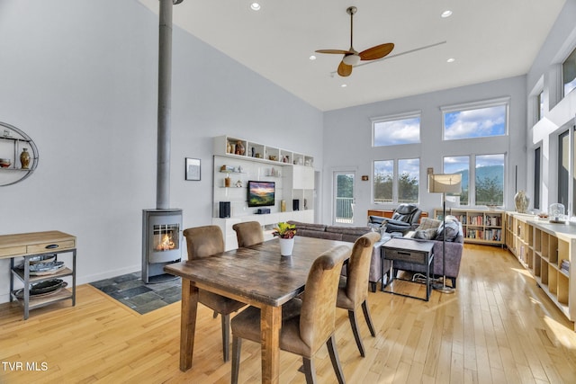 dining area featuring a high ceiling, light wood finished floors, ceiling fan, and a wood stove