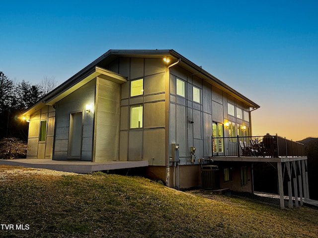 back of house at dusk with central AC, a wooden deck, board and batten siding, and a yard