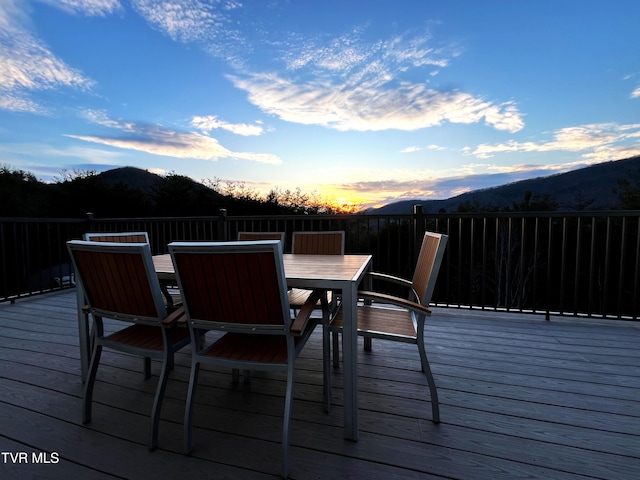 deck at dusk with outdoor dining area and a mountain view