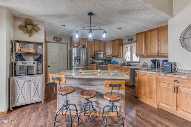 kitchen featuring a kitchen bar, dark wood-style flooring, stainless steel appliances, a textured ceiling, and a sink