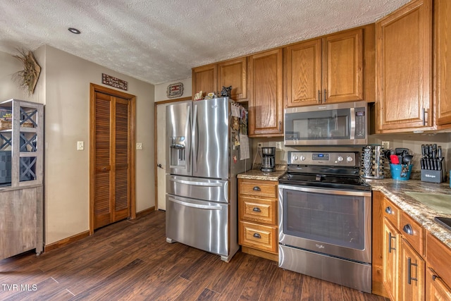 kitchen featuring dark wood-style flooring, stainless steel appliances, light stone counters, and brown cabinets