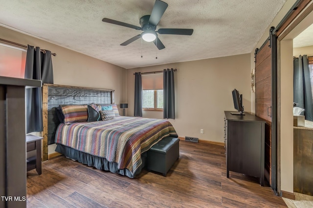 bedroom with dark wood-type flooring, a barn door, visible vents, and baseboards
