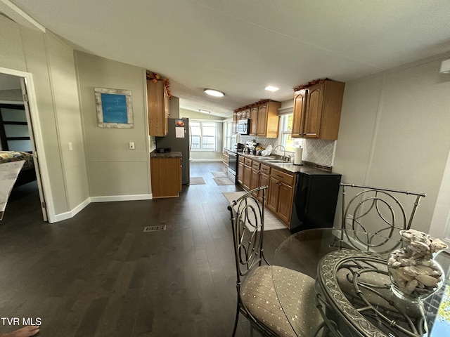 kitchen featuring stainless steel appliances, tasteful backsplash, a sink, vaulted ceiling, and brown cabinetry