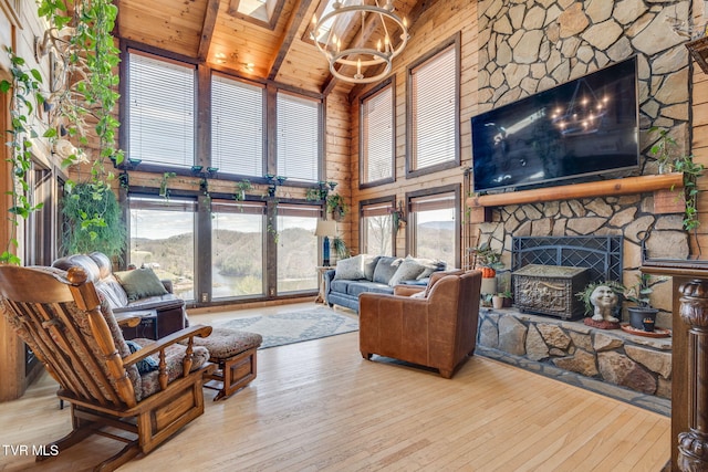 living area featuring a chandelier, a stone fireplace, beam ceiling, wooden ceiling, and wood-type flooring