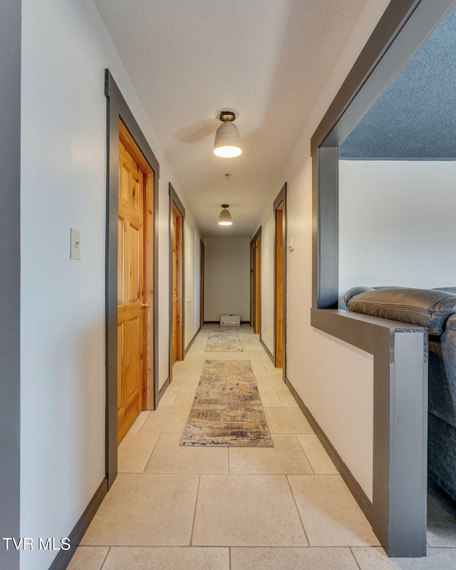 hall with light tile patterned floors, baseboards, and a textured ceiling