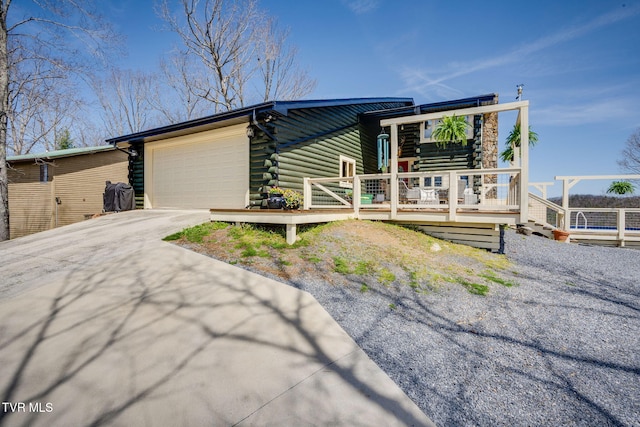 view of front facade featuring log siding, concrete driveway, a deck, and an attached garage
