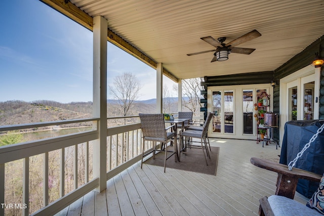 deck with french doors, outdoor dining area, a mountain view, and ceiling fan