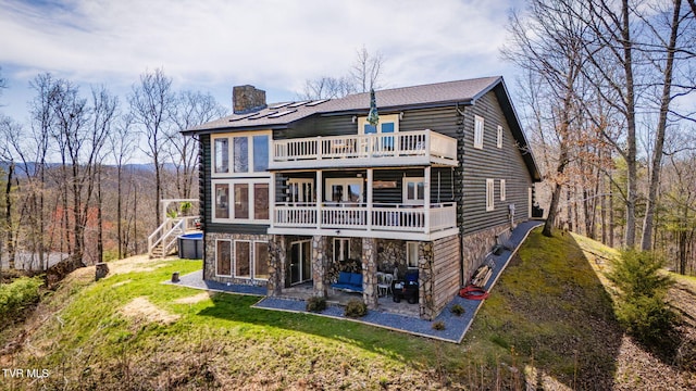 rear view of property with a lawn, stone siding, a patio, a balcony, and a chimney