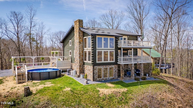 back of house with a chimney, a deck, central AC unit, a lawn, and an outdoor pool