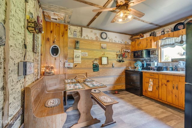 kitchen featuring wood walls, light wood-style floors, a ceiling fan, black appliances, and brown cabinets