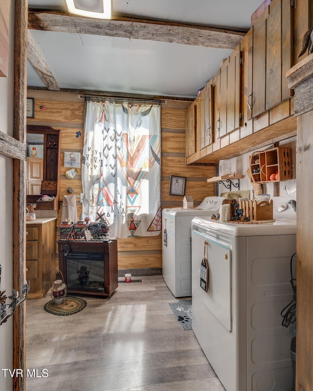 clothes washing area featuring wood walls, independent washer and dryer, light wood-style floors, visible vents, and cabinet space