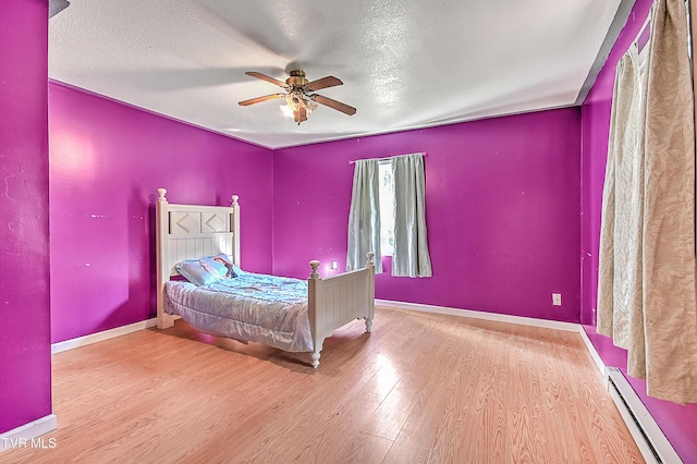 bedroom with a ceiling fan, wood finished floors, a textured ceiling, a baseboard radiator, and baseboards