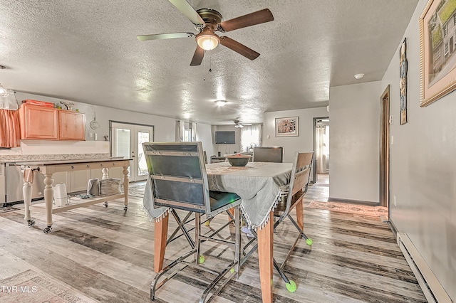 dining room with light wood-style flooring, a ceiling fan, a baseboard heating unit, and a textured ceiling