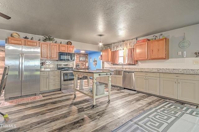 kitchen featuring a sink, a textured ceiling, stainless steel appliances, light wood-style floors, and decorative backsplash