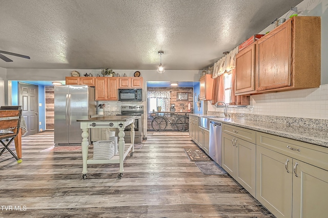 kitchen with ceiling fan, wood finished floors, stainless steel appliances, a sink, and backsplash