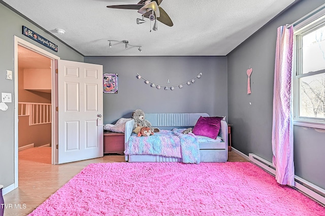 bedroom with a textured ceiling, wood finished floors, multiple windows, and a baseboard radiator