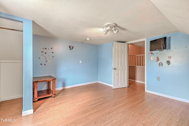 unfurnished living room with baseboards, light wood-style floors, lofted ceiling, and a textured ceiling