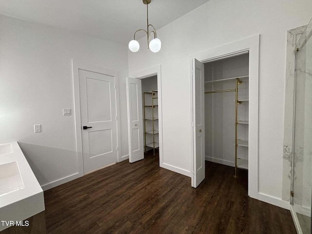 unfurnished bedroom featuring a spacious closet, a notable chandelier, baseboards, and wood finished floors