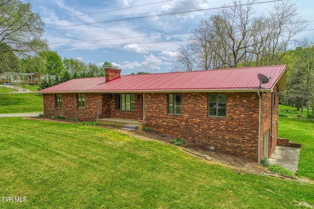 view of front of house featuring a chimney, metal roof, brick siding, and a front lawn