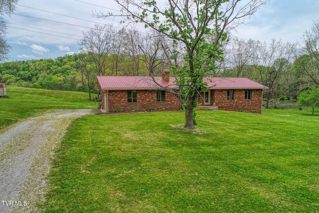 single story home featuring brick siding, a front lawn, driveway, and a view of trees